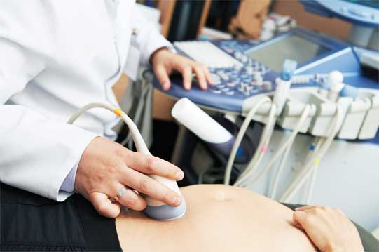 Closeup of an ultrasound device on a pregnant woman's abdomen